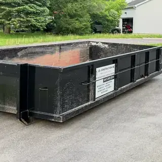 Empty black I.D. Construction roll-off bin on a driveway, company sign on the side