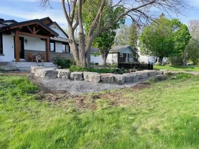 Side view of an armour stone wall and gravel bed around a front-yard tree