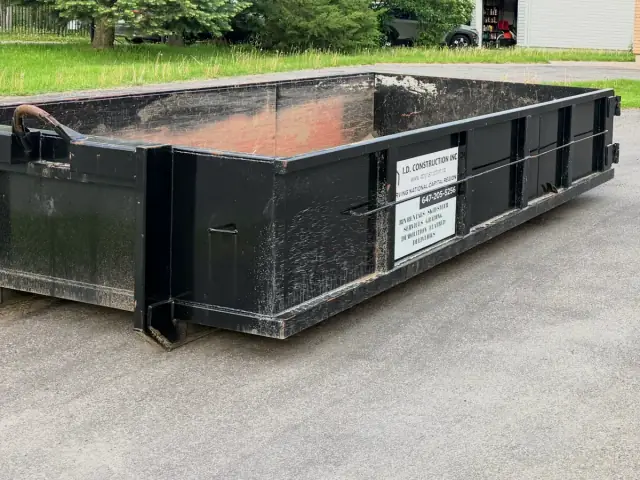 Conteneur noir vide d’I.D. Construction dans une entrée, enseigne de l’entreprise sur le côté