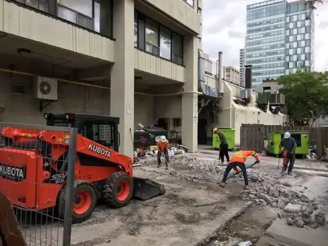 Kubota skid steer and crew breaking out a concrete slab beside an apartment building