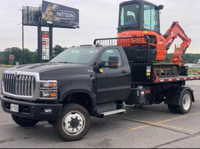 Camion plateau noir transportant une mini-excavatrice Kubota U35