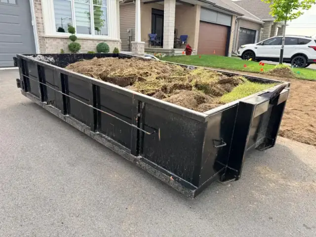 Black roll-off bin filled with stripped sod on a residential driveway