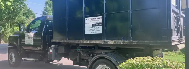 Camion à bras d’I.D. Construction transportant un conteneur noir avec l’enseigne et le numéro de l’entreprise