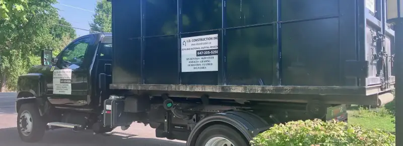 I.D. Construction hook-lift truck carrying a black roll-off bin with the company sign and phone number