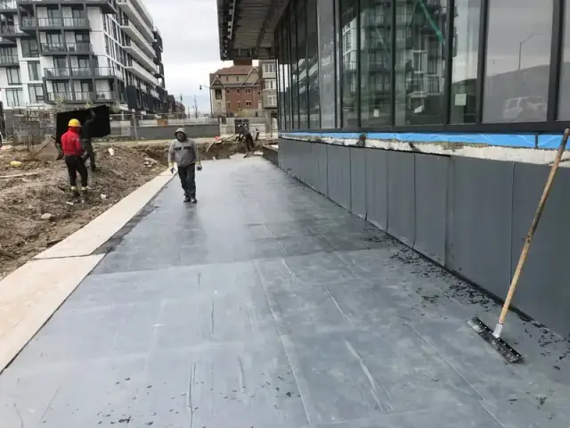 Waterproofing membrane on a walkway deck along a glass building face