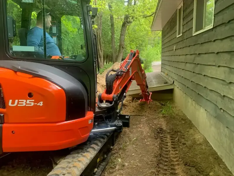 Kubota mini excavator digging along a house foundation wall