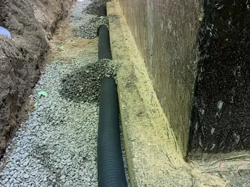 Perforated weeping tile laid on clear stone at the base of a foundation wall