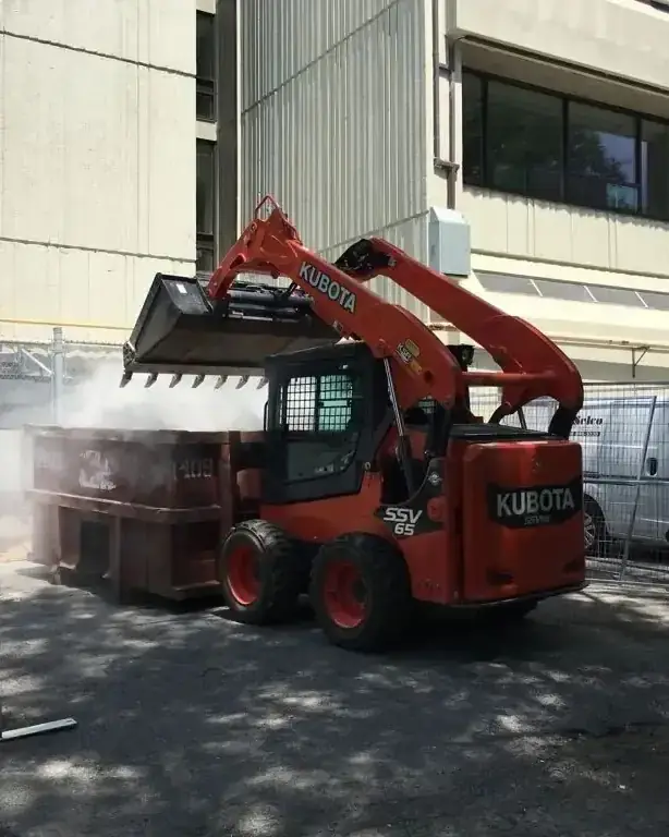 Skid steer loading debris into a bin with water spray keeping dust down