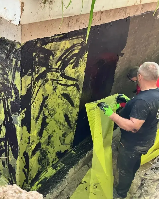 Ouvrier appliquant une membrane et un tissu d’armature sur le mur extérieur d’une fondation
